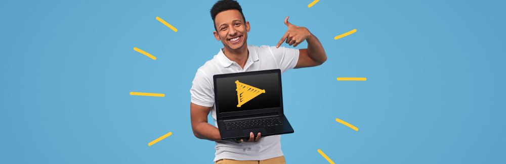 Smiling man in a white shirt holding an open laptop and showing us a yellow "play" video button on the screen.