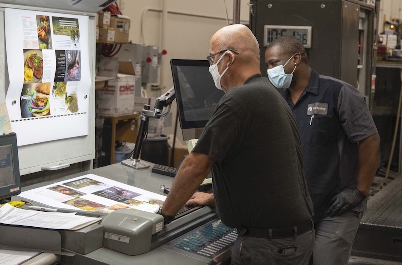 two print production team members discussing a project.