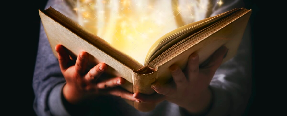 Person holding a book open to center page with light illuminating the book.