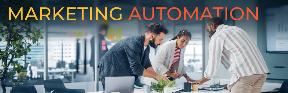 Three professionals dressed in business casual clothing that are leaning over a table, planning. Words on image read Marketing Automation